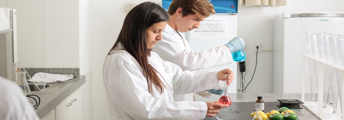 <p>Homem e mulher observando frascos em laboratório</p>
